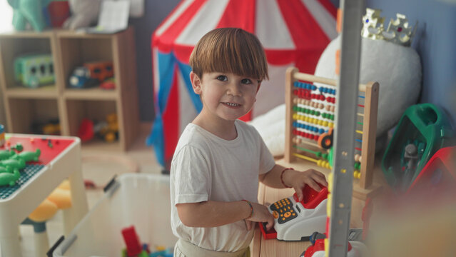 Boy playing with toy cash register and abacus pressing buttons and smiling inside building; curiosity joy.