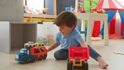 Fotobehang Lego Boy playing with toy trucks and pushing a loader while reaching and arranging vehicles in a kids play area inside a building  playful curiosity.  © Krakenimages.com