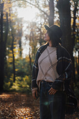 Profile portrait of thoughtful mature Caucasian woman in hat and blanket standing in backlight of autumn sun. © olezzo