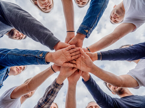 ow angle view of diverse young people putting hands together in teamwork huddle