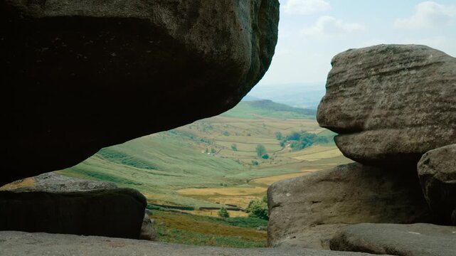 Valley landscape framed by massive granite boulders. Natural rock window overlooking patchwork fields and rolling countryside. Scenic geological formation with rugged stone and distant rural panorama
