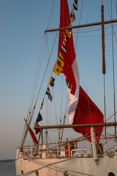Sailing ship displays flags in the evening sky by the waterfront. A sailing ship shows colorful flags and red sails during the evening near the water.