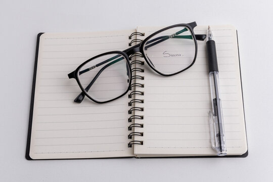 Spiral notebook with Success text pena and eyeglasses on white background