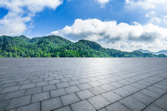 Empty paved plaza floor and green mountains under blue sky as background