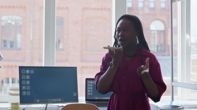 Young African American woman recording voice message on smartphone in modern office. Footage is ideal for corporate communication and mobile business technology promos