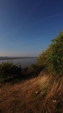 Vertical golden river banks of the Mersey overlooking Runcorn industrial sunlit coastline horizon