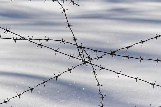 Sharp rusty barbed wire fence crossing in a cold winter setting, creating a sense of confinement and harsh industrial isolation against a soft snowy backdrop at an abandoned site