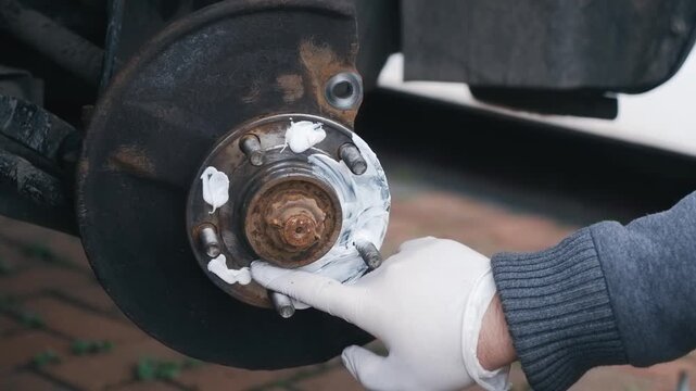 Applying graphite anti seize grease to wheel hub surface during brake assembly. Protective lubrication preventing corrosion and future component seizure on hub contact area. DIY automotive maintenance