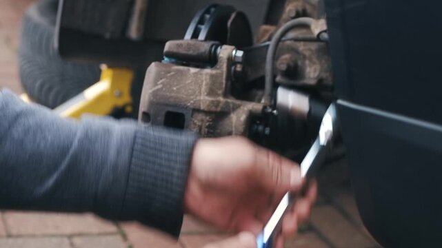 Torque wrench securing caliper guide pins during passenger car brake reassembly. Mechanic applying precise fastening force on braking components during automotive maintenance. Safety focused