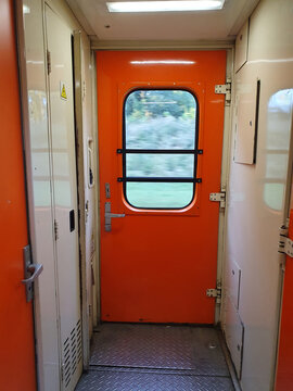 Bright orange exit door inside a passenger train carriage with window view of motion landscape