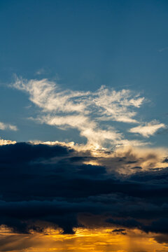 Dramatic sunset with dark storm clouds and golden light. Beautiful sunset sky with bright golden sunbeams breaking through dark heavy clouds under blue sky