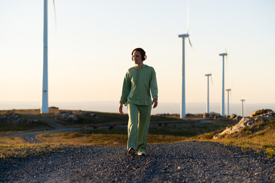 A white woman walking near wind turbines at sunset in Galicia Spain