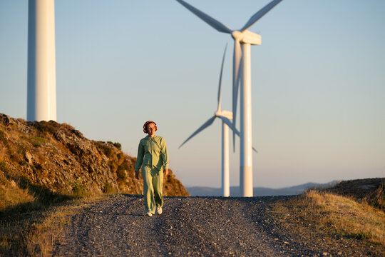 A white woman in a green tracksuit walks near wind turbines in Galicia