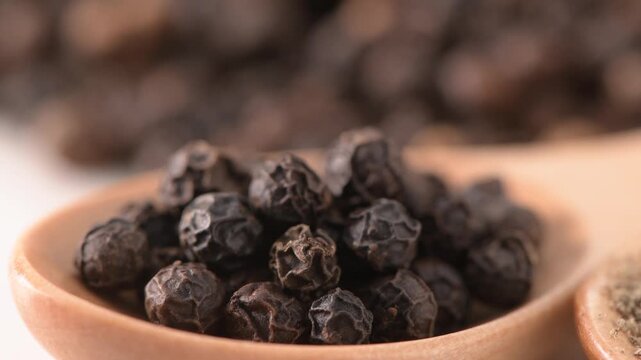 Pile of whole black peppercorns on white background