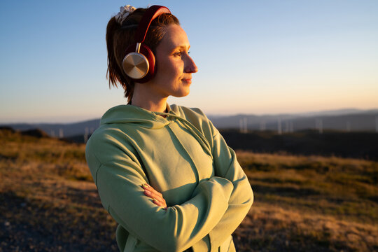 A white woman wearing headphones enjoys the sunset outdoors