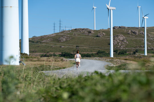 A white woman running on a gravel path near wind turbines in Galicia