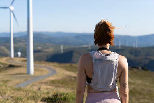 A white woman with a backpack observes wind turbines