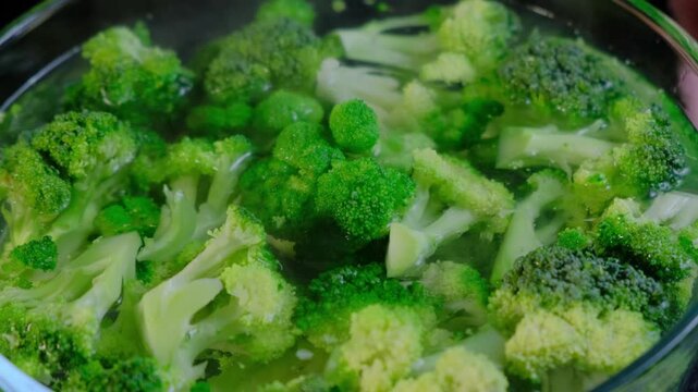 Close-up overhead view of chopped broccoli florets and stems submerged in greenish liquid in a glass bowl, Cooking.