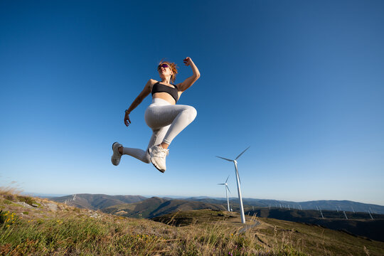 White Woman jumping actively outdoors near wind turbines in Galicia