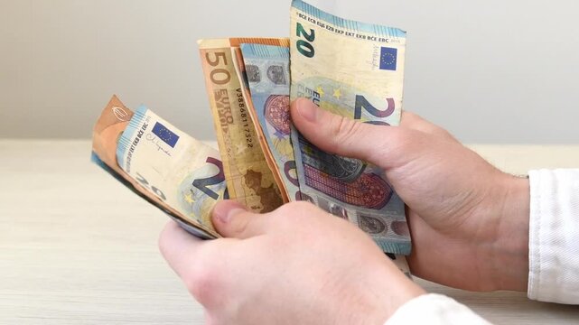 A close-up of a man's hands counting a stack of euro banknotes. Successful business deals, cost control, debt repayment, lending, borrowing money, corruption, bribery.