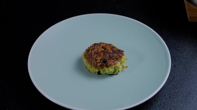 Close-up of a hand using a fork to place a deep-fried food item onto a mint green ceramic plate during cooking, indoors.