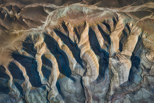 Aerial view of striped badlands ridges casting long shadows where erosion has carved fine drainage channels