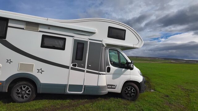 A white camper parked on a bright green grass field near the beautiful Paravani Lake in Georgia with a stunning mountain landscape in the background, showcasing a scenic vacation and the concept of fr