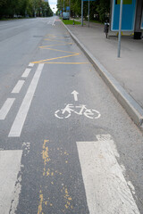 Fototapeta premium A bicycle lane is marked on the street. The lane has a bike symbol with an arrow pointing forward. Surrounding areas include parked cars and a bus stop nearby.
