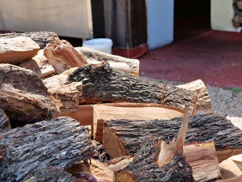 Close-up of Split Firewood Logs - A closer, lower-angle shot of the firewood pile from image_10, focusing on individual logs in the foreground. Blurred background elements like a white bucket