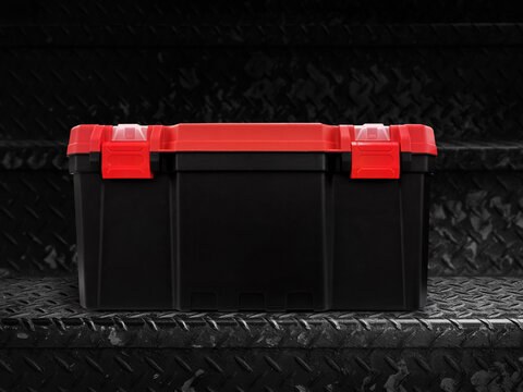 A black and red plastic storage box is placed on a black metal plate.