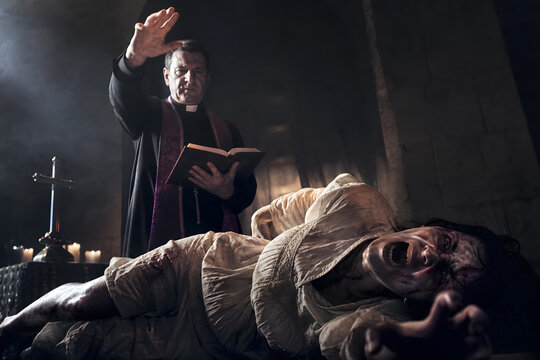Priest performing exorcism ritual with bible over a screaming possessed person in dark candlelit room