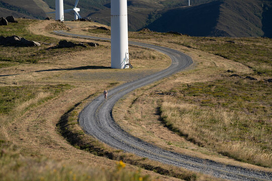 A white woman trail runs along a winding path beside wind turbines