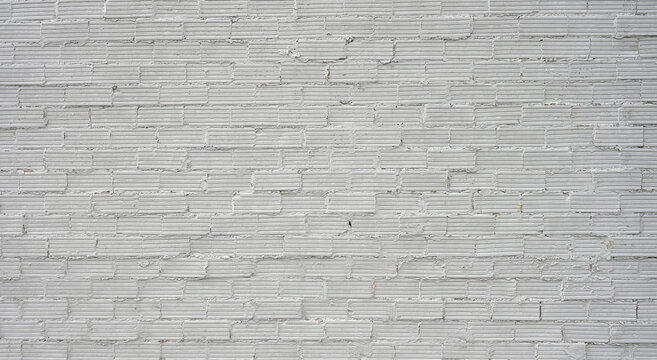 Horizontal rough white painted brick and mortar wall surface with uneven protruding bricks, overfilled joints, chipped flaking mortar and uniform grooved brick texture