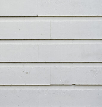Vertical view of white painted concrete clapboard texture with flat smooth board faces, shallow uniform lap lines, caulked grooves, surface knicks, weathering, and chipped paint