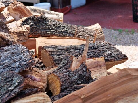 Close-up of Split Firewood Logs - A closer, lower-angle, focusing on individual logs in the foreground. Blurred background elements like a white bucket, a metal table, and a red surface 