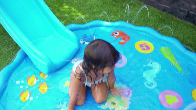 Little girl playing on inflatable water slide in the backyard