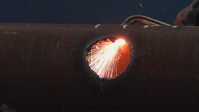 Close-up thermal cutting of rusted steel pipe with bright sparks, molten edge glow and corroded surface detail in dark industrial workshop scene, with cutting, spark, torch, pipe detail