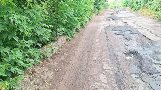 Damaged country road with cracks and potholes, POV driving forward, infrastructure and rural road maintenance concept for local government and news