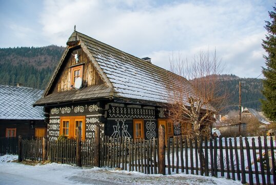 Traditional wooden house in the historic village of Cicmany, Slovakia, decorated with distinctive white folk ornaments and surrounded by snow-covered countryside and forested mountains.