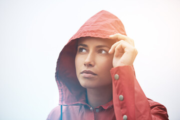 Fototapeta premium Woman, rain jacket and thinking with hood for weather, cloudy sky or winter season in outdoor storm. Face of female person with red waterproof coat in wonder for rainy overcast or fog on mockup space