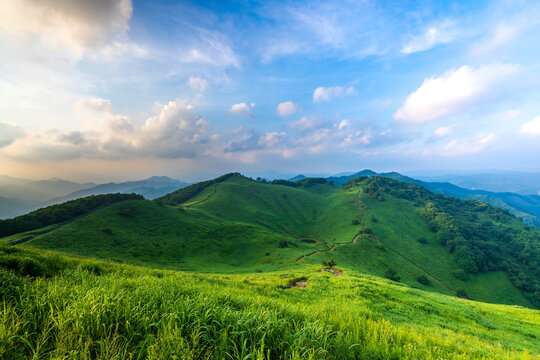 Panoramic view of a lush green karst doline and hiking trails on the ridge of Mindungsan Mountain under a bright sky, Jeongseon, South Korea.