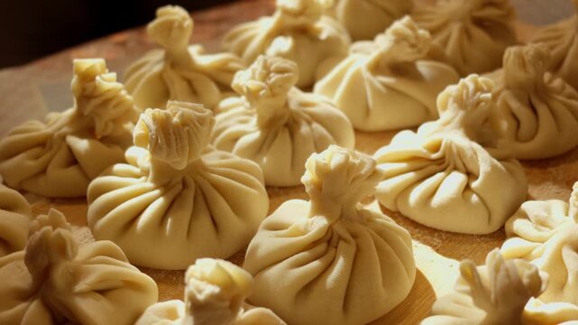 Slow camera movement across rows of fresh uncooked Georgian khinkali dumplings resting on rustic wooden board in soft side light, capturing authentic Eastern European culinary heritage.