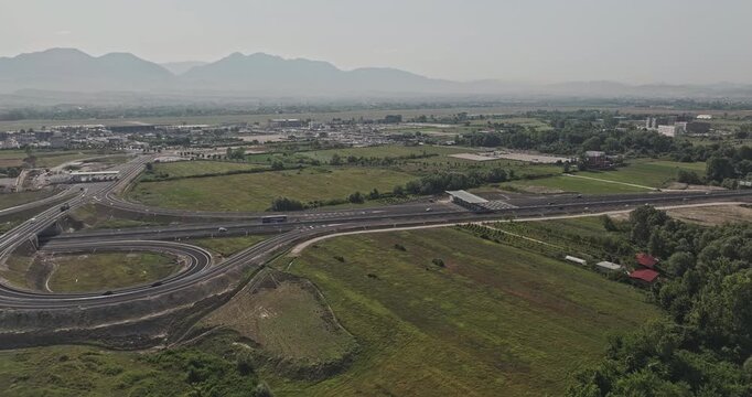 Tirane Albania Aerial v3 low flyover above the highway interchange near Nd&euml;rmjet&euml;s, revealing farmland, scattered homes and Rinas airport landscape - Shot with Mavic 3 Pro Cine - July 10th 2024