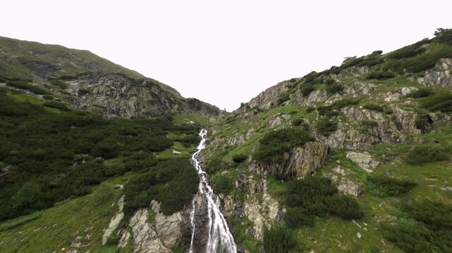 A scenic mountain waterfall cascades down rocky slopes into the turquoise waters of Barbellino Lake near the Serio Dam in Italy.