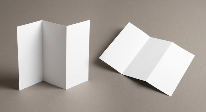 Two blank white tri-fold brochures lie partially unfolded on a warm gray surface under soft studio lighting, serving as a clean minimalist presentation template.
