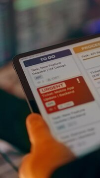 Agile trello task board workspace urgent ticket user interface tablet. Close-up hand holding tablet display showing project management workflow dashboard, software development tickets