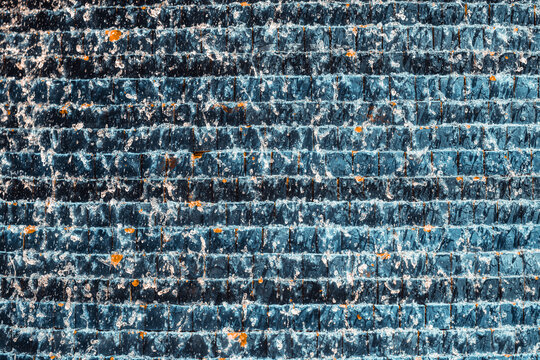 Close-up texture of clear fountain water cascading and splashing across rows of dark blue square tiles, accented by scattered orange leaves and sparkling droplets