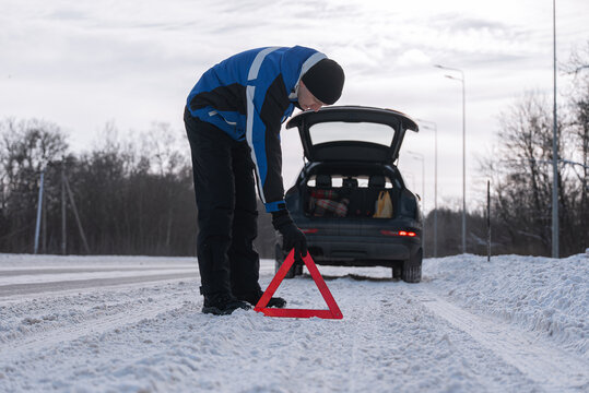 Driver place warning triangle beside car on snowy roadside
