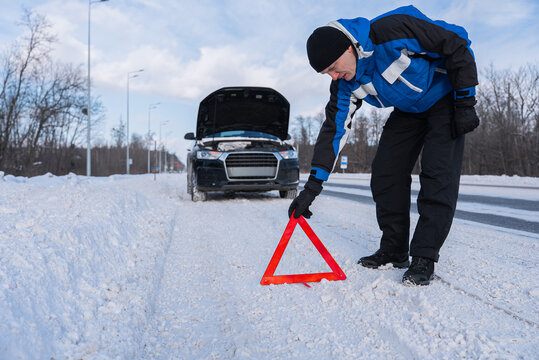 Driver place warning triangle near broken car on winter road