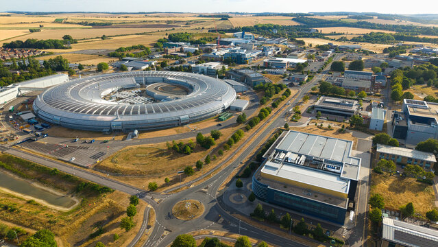 Aerial view of the Diamond Light Source synchrotron, featuring its circular building, modern research laboratories, and green fields in Harwell Oxford, England, United Kingdom.